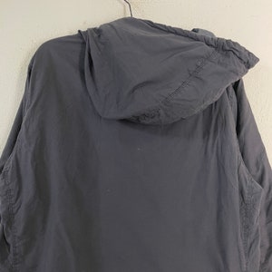 Pode incluir: Casaco cinza escuro com capuz, com z&iacute;per completo e capuz. O casaco &eacute; feito de um material leve e tem um design simples e minimalista. O capuz &eacute; preso ao casaco e foi projetado para proteger contra os elementos.