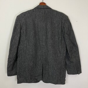 Op de afbeelding: Een donkergrijze blazer met een textuurpatroon. De blazer heeft een enkele knoopsluiting en lange mouwen.