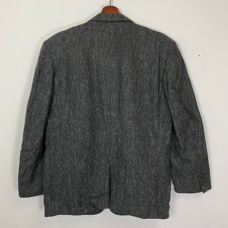 Op de afbeelding: Een donkergrijze blazer met een textuurpatroon. De blazer heeft een enkele knoopsluiting en lange mouwen.