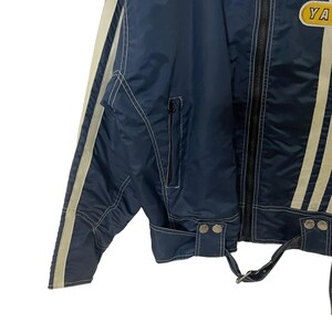 May include: A blue and white striped jacket with a zipper closure and a yellow patch with the word "YA" on it. The jacket has white piping and a white stripe down each sleeve.