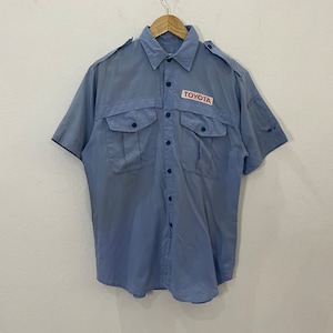 May include: A light blue short-sleeved button-down shirt with two chest pockets and a patch on the left chest that says "TOYOTA" in red letters.