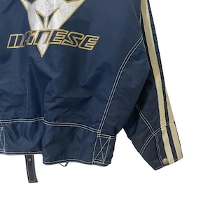 May include: A navy blue jacket with white stitching and white stripes on the sleeves. The jacket has a gold logo that says "Dainese" on the back.