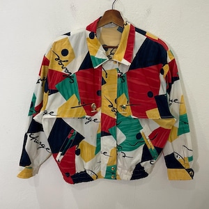 Puede incluir: Una chaqueta colorida con estampado geométrico sobre fondo blanco. La chaqueta tiene cierre de cremallera y cuello alto. El estampado incluye rojo, amarillo, verde, azul y negro.