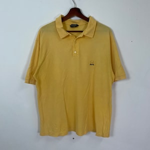 Può includere: Una polo a maniche corte gialla con un piccolo logo ricamato sul petto sinistro.