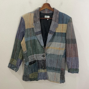 May include: A multi-colored plaid blazer with a single button closure. The blazer has a patch pocket on the left side and a woven label that reads "SAO".