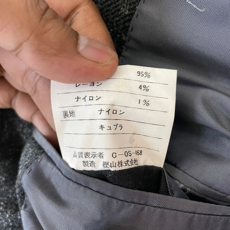 Op de afbeelding: Een wit label met zwarte tekst die de stofsamenstelling van een kledingstuk beschrijft. Het label vermeldt: 95% rayon, 4% nylon, 1% nylon. Het label bevat ook de tekst "C-OS-468" en "樫山株式会社" (Kashiyama Corporation).
