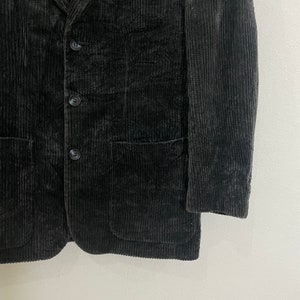 以下が含まれることがあります： ノッチドラペルと3つのボタン留めが特徴のダークグレーのコーデュロイブレザー。ブレザーには、前面にフラップポケットが2つ、カフスにボタンが1つずつ付いています。