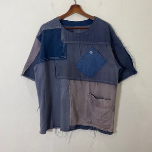 May include: A blue and gray patchwork short-sleeved shirt with multiple pockets. The shirt has a distressed look with frayed edges.