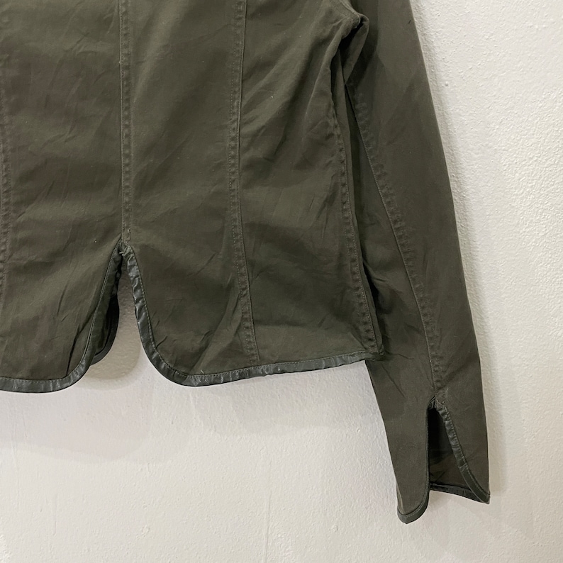 May include: A dark green utility jacket with a long sleeve and a black trim around the bottom and cuffs.