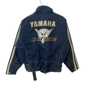 May include: A navy blue jacket with white stripes down the sleeves. The jacket has a zipper closure and a large Yamaha Dainese logo on the back.