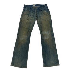 Puede incluir: Vaqueros de mezclilla azul desgastados con detalles descoloridos y rotos. Los vaqueros tienen un corte recto y un diseño clásico de cinco bolsillos.