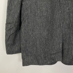 Op de afbeelding: Een donkergrijze blazer met een textuur, geweven stof. De blazer heeft een klassieke, getailleerde pasvorm.