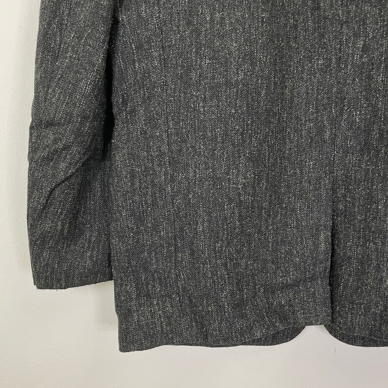 Op de afbeelding: Een donkergrijze blazer met een textuur, geweven stof. De blazer heeft een klassieke, getailleerde pasvorm.