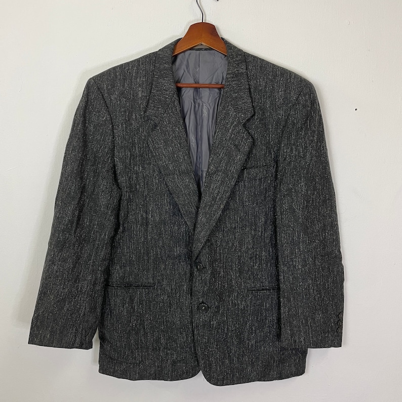 Op de afbeelding: Een grijs blazer met een textuurpatroon. De blazer heeft een knoopsluiting met twee knopen en twee zakken.