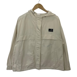 May include: A beige hooded jacket with a zip fastening and two front pockets. The jacket features a small black square patch on the right side with a logo. The jacket is hanging on a wooden hanger.