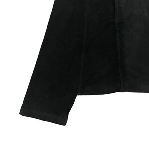 Puede incluir: Una chaqueta de ante negra con una silueta larga y ajustada. La chaqueta tiene un dise&ntilde;o sencillo con un cuello puntiagudo y un cierre de bot&oacute;n &uacute;nico.