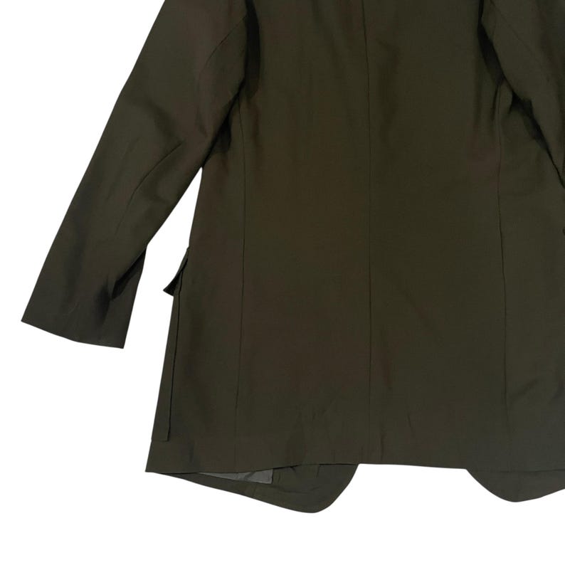 Puede incluir: Una americana de color verde oliva con mangas largas, cuello estructurado y un bolsillo lateral con solapa. La prenda est&aacute; confeccionada con costuras verticales en la espalda y los costados, mostrando un acabado de tela lisa y uniforme.