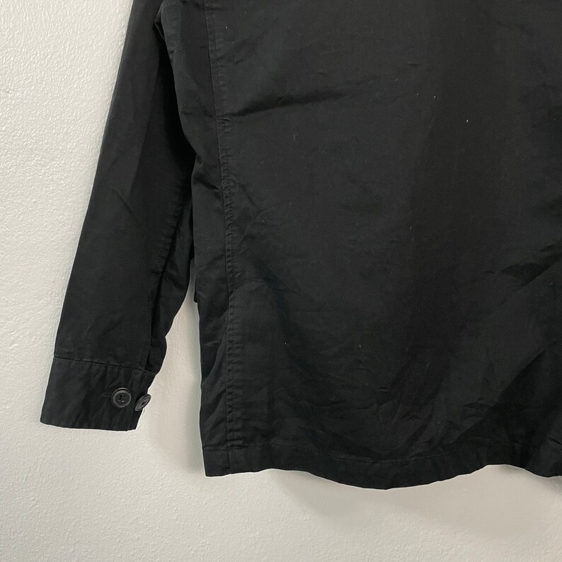 May include: Black jacket with long sleeves and a buttoned cuff. The jacket has a classic design with a tailored fit. The fabric appears to be a smooth, solid color. The buttons are dark and round.