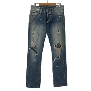 May include: Distressed blue denim jeans with multiple rips and tears throughout the fabric. The jeans have a straight leg fit and a button fly closure.