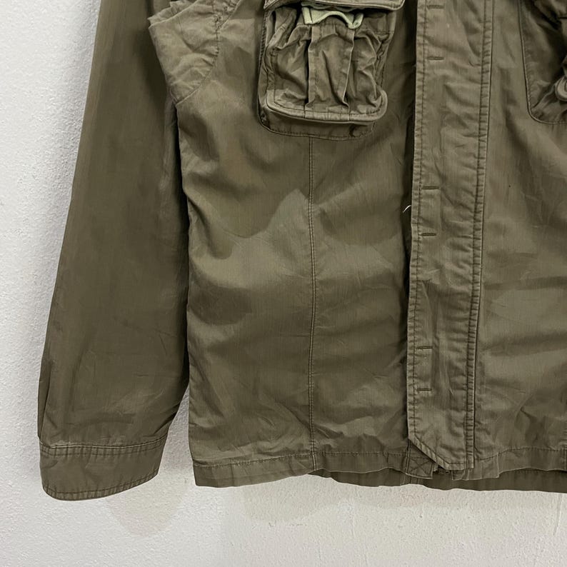 May include: Olive green jacket with multiple pockets and a button-up front. The jacket has a classic design with a tailored fit, suitable for various occasions. The fabric appears to be a lightweight material, ideal for layering.
