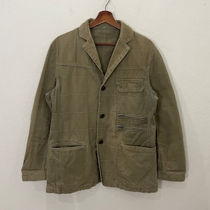 Puede incluir: Una chaqueta de color verde oliva con un patrón de cuadrícula, solapa de muesca y tres botones frontales. La prenda incluye un bolsillo en el pecho con solapa, dos bolsillos horizontales con cremallera y dos bolsillos grandes.