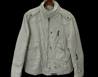 May include: A light gray zip-up jacket with multiple pockets and a black zipper. The jacket has a stand-up collar and a black label that reads "DSQUARED2".