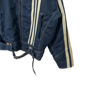 May include: A navy blue jacket with white stripes down the sleeves and sides. The jacket has a zipper closure and a belt at the waist.