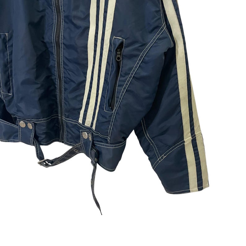 May include: A navy blue jacket with white stripes down the sleeves and sides. The jacket has a zipper closure and a belt at the waist.