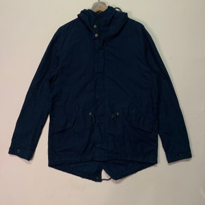 May include: A navy blue hooded jacket with a drawstring waist and two front pockets. The jacket has a button-up front and a hood with two buttons. The jacket is hanging on a wooden hanger.
