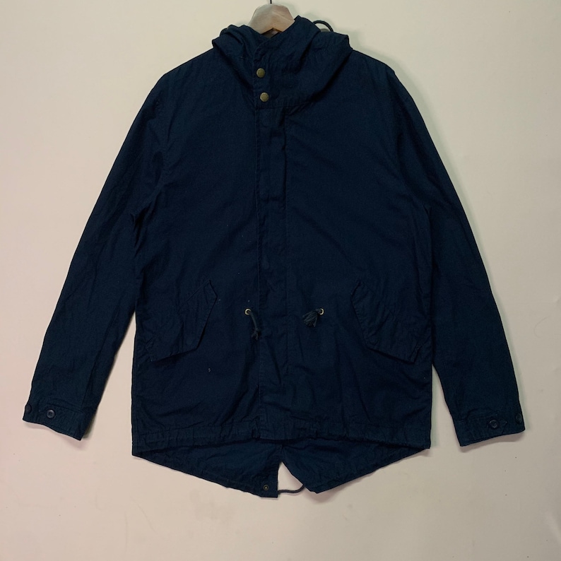 May include: A navy blue hooded jacket with a drawstring waist and two front pockets. The jacket has a button-up front and a hood with two buttons. The jacket is hanging on a wooden hanger.