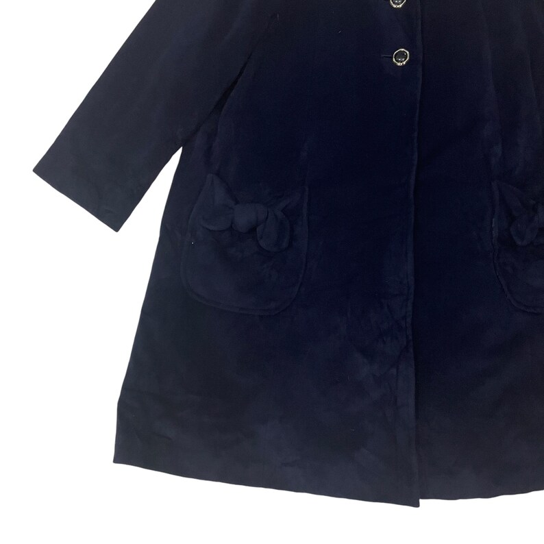 May include: A navy blue velvet coat with a single button closure and two pockets with decorative bows. The coat has a long, flowing silhouette.