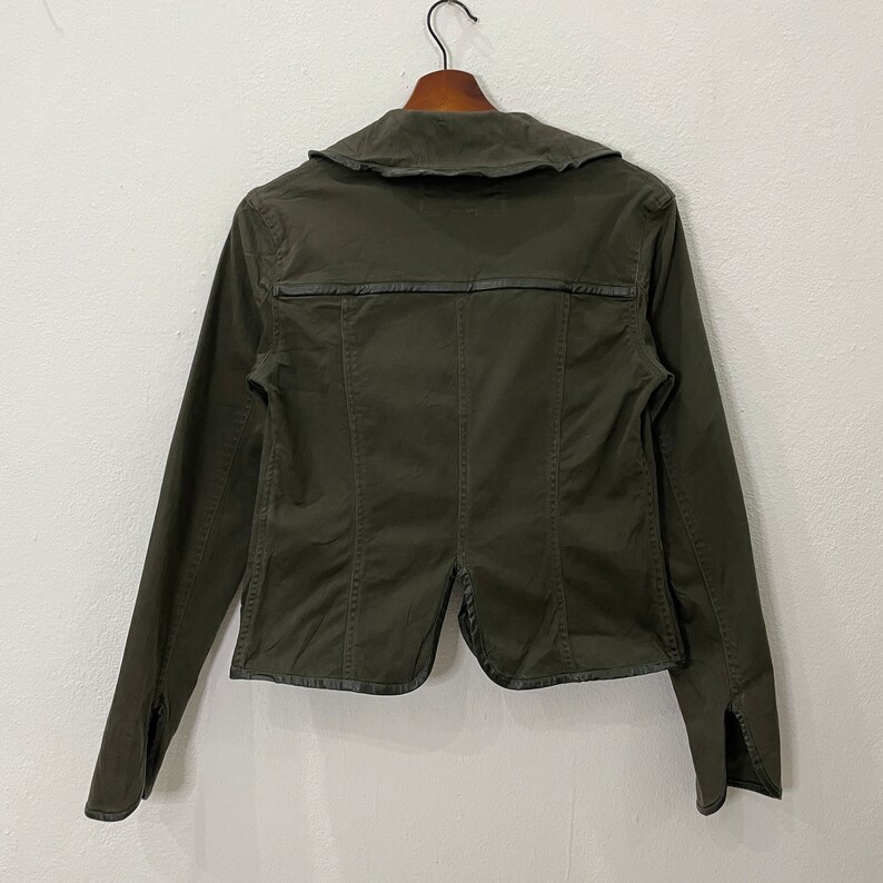 May include: A dark green utility jacket with a collar and long sleeves. The jacket has a zipper closure and a flap pocket on the chest.