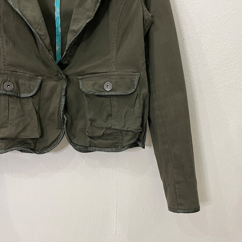 May include: A dark green cropped blazer with a collar, two pockets, and a button closure. The blazer has a slightly distressed look and is made of a soft, comfortable fabric.