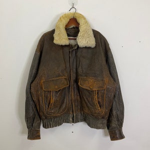 May include: A brown leather bomber jacket with a shearling collar. The jacket has two large pockets on the front and a zipper closure.