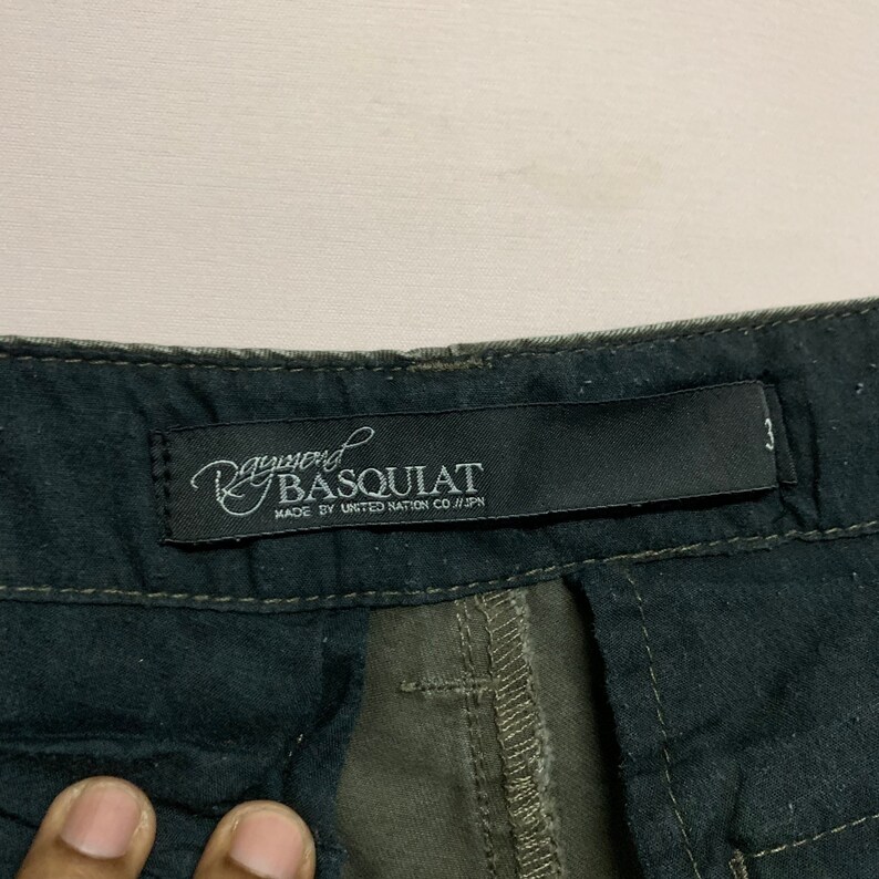 May include: A black and green cargo pants label with the text "Ray-nerd Basquiat Made by United Nation Co. // JPN"