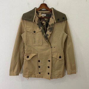 May include: A tan double-breasted jacket with a camouflage lining and a brown corduroy collar. The jacket has two large pockets on the front and a smaller pocket on the left chest. The jacket is distressed and has a vintage look.