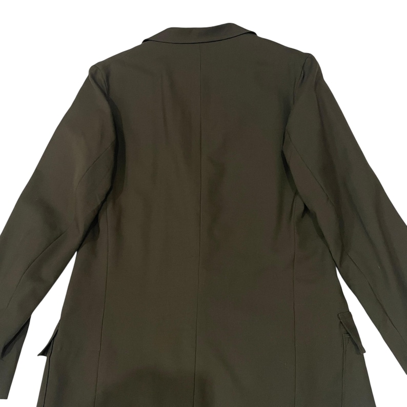 Puede incluir: Un blazer de color verde oliva s&oacute;lido que presenta un cuello con solapa de muesca, mangas largas y dos bolsillos con solapa situados en la parte inferior frontal. La prenda tiene una costura vertical central en la espalda y hombros.