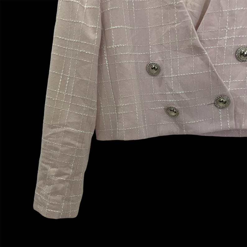 May include: A pink blazer with a white grid pattern and silver buttons. The blazer has a double-breasted closure and long sleeves.