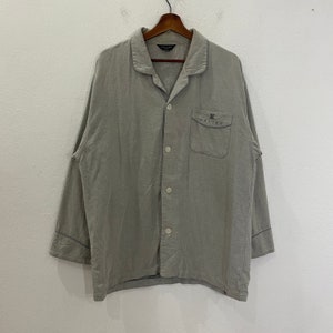 Puede incluir: Una camisa gris de manga larga con botones, un bolsillo en el pecho y el texto "CELINE" bordado en el bolsillo.