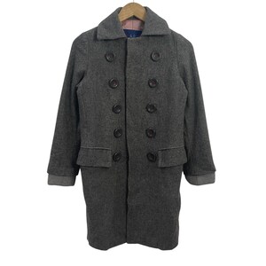 May include: A gray wool coat with a double-breasted design. The coat features large, dark buttons, two front pockets, and a notched collar. The cuffs are a lighter gray. The coat is hanging on a wooden hanger.