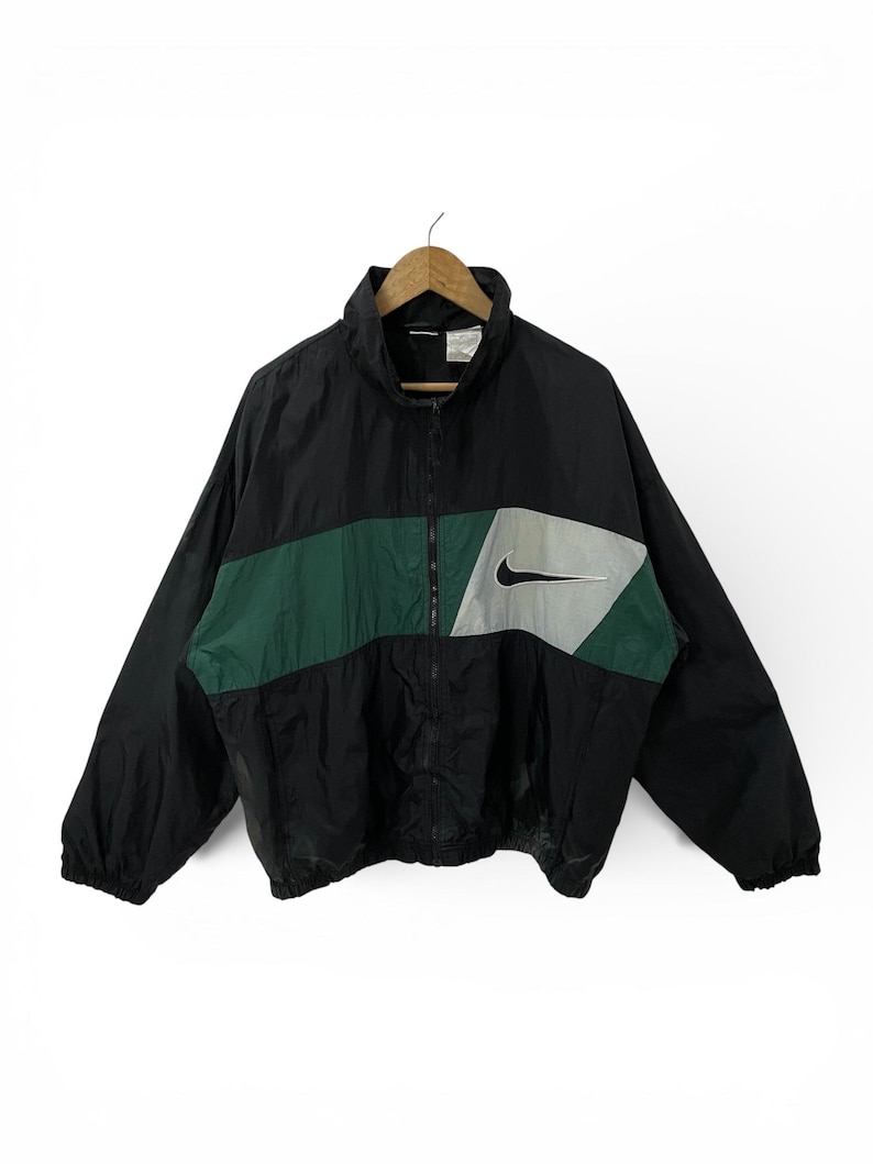 May include: Black and green Nike windbreaker jacket with a full zipper closure. The jacket features a color block design with a green stripe across the chest and a gray and black Nike swoosh logo.