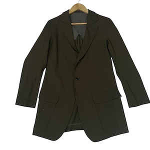 Puede incluir: Un blazer de color marr&oacute;n oscuro con solapa de muesca, cierre frontal de un solo bot&oacute;n y dos bolsillos grandes con solapa en la cintura. La prenda se muestra en una percha de madera, con mangas largas y una silueta estructurada.