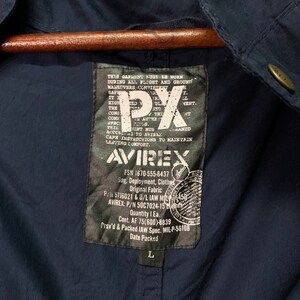 May include: Navy blue jacket with a label featuring the text "AVIREX" and "PX". The label also includes text about garment care and specifications. The jacket is hanging on a wooden hanger.