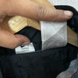 May include: Close-up of a black garment's interior, featuring a white tag with care instructions and the Nike logo. The tag includes the RN and CA numbers. The garment appears to be made of a dark, possibly quilted material.
