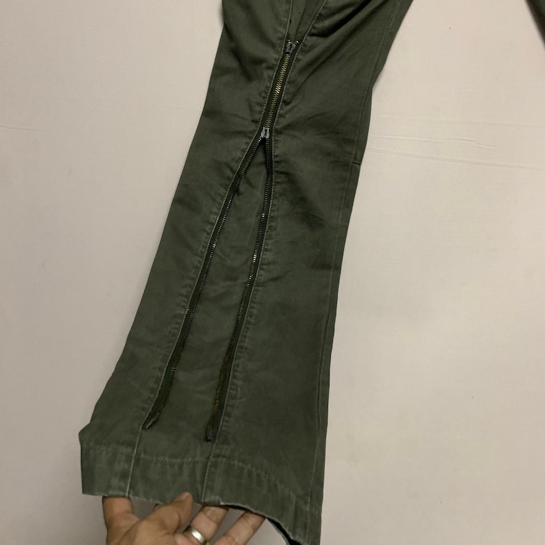 May include: A pair of green cargo pants with two long zippers running down the outside seams of each leg.