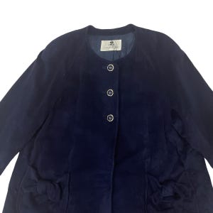May include: A navy blue corduroy jacket with a round neckline and five buttons down the front. The jacket has two pockets on the front with bows on the sides. The label on the inside of the jacket reads "Country Style".