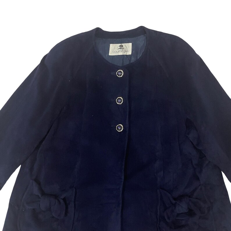 May include: A navy blue corduroy jacket with a round neckline and five buttons down the front. The jacket has two pockets on the front with bows on the sides. The label on the inside of the jacket reads "Country Style".