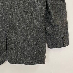 Op de afbeelding: Een donkergrijze blazer van een getextureerde stof. De blazer heeft een enkele knoopsluiting en twee zakken aan de voorkant.