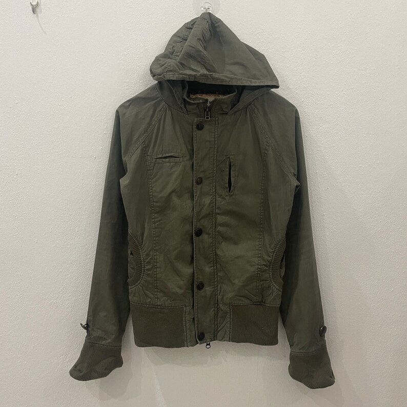 May include: A green hooded jacket with a zipper and button closure. The jacket has a ribbed hem and cuffs.