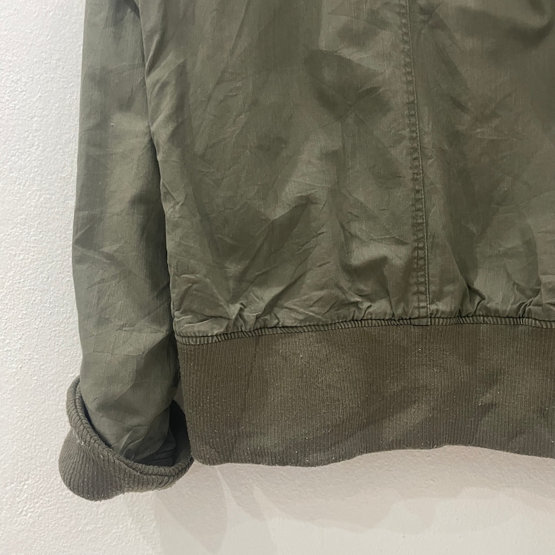 May include: A green cotton jacket with a ribbed knit bottom band. The jacket has a zipper closure and long sleeves.